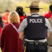 Un policier en uniforme vêtu d'un gilet portant l'inscription « POLICE » est à l'extérieur avec un groupe de personnes vêtues de chandails rouges.