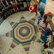 Un groupe de personnes se tiennent debout et forment un cercle dans un grand espace intérieur au plancher carrelé. Plusieurs personnes sont vêtues d'uniformes officiels et tiennent des drapeaux.