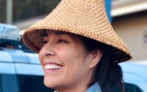Indigenous woman in a cedar hat smiles at something off-camera
