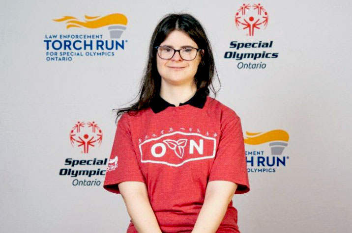A woman in a red T-shirt sits smiling at the camera