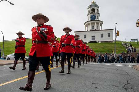 Plusieurs agents de la GRC en tunique rouge marchent le long d’une rue du centre-ville d’Halifax. L’horloge de la ville et les membres d’un autre service de police sont en arrière-plan.