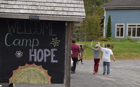 Des enfants non identifiables jouent à l'arrière-plan d'une pancarte sur laquelle on peut lire : Bienvenue au Camp Hope.