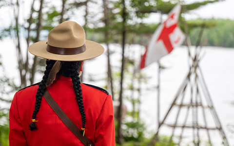 Un officier de la GRC en tunique rouge, dos à la caméra, regarde un drapeau du Grand Conseil de la Nation Mi'kmaq.