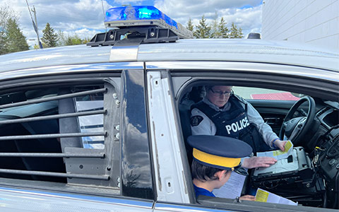 Un officier de la GRC et un enfant non identifiable assis dans une voiture de police regardant des documents.