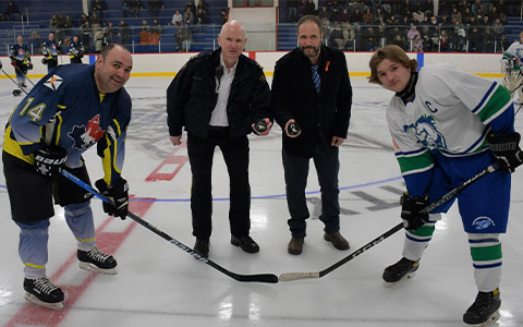 Deux joueurs de hockey et deux officiels sourient à la caméra avant la mise au jeu.