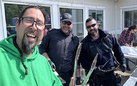 Deux policiers et un membre de la communauté sourient à la caméra alors qu'ils se tiennent derrière un barbecue.