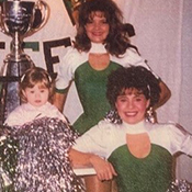Deux meneuses de claque posent pour la photo avec des pompons. Une jeune enfant est assise dans l'énorme Coupe Grey qui se trouve entre elles. 