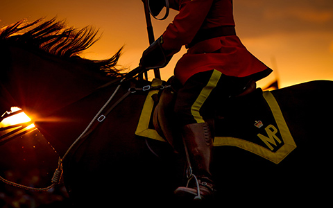 A police officer in red serge rides a black horse as the sun sets behind them