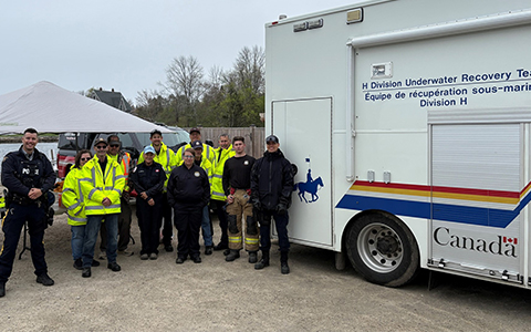 RCMP officers and firefighters stand alongside the RCMP Underwater Recovery Team’s vehicle.