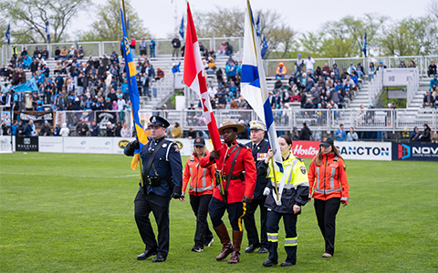 First responders, including an RCMP officer in red serge, carry flags on a field.