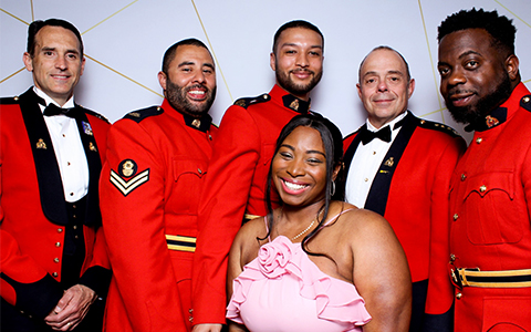 Five uniformed police officers stand with a woman in a pink ball gown.