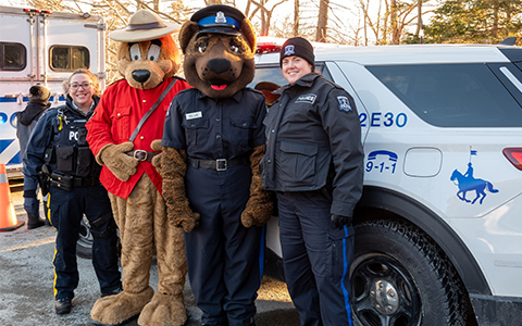An RCMP officer and a Halifax Regional Police officer stand with mascots in front of a police vehicle.