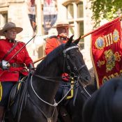 Deux gendarmes à cheval. La femme porte une épée et l'homme un drapeau sur lequel figurent les armoiries des régiments de la <abbr>GRC</abbr>.