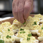 A cook garnishes a tray of devilled eggs.