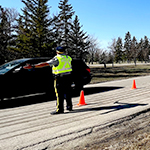 A cadet directs traffic on a summer day. There are bright orange pylons and the cadet wears a high visibility vest.