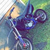 A blue and black dirt bike leaning against the foundation of a structure.