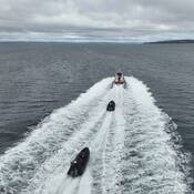 A large Canada Coast Guard vessel is underway on the ocean and two RCMP Zodiac vessels follow closely behind in its wake.