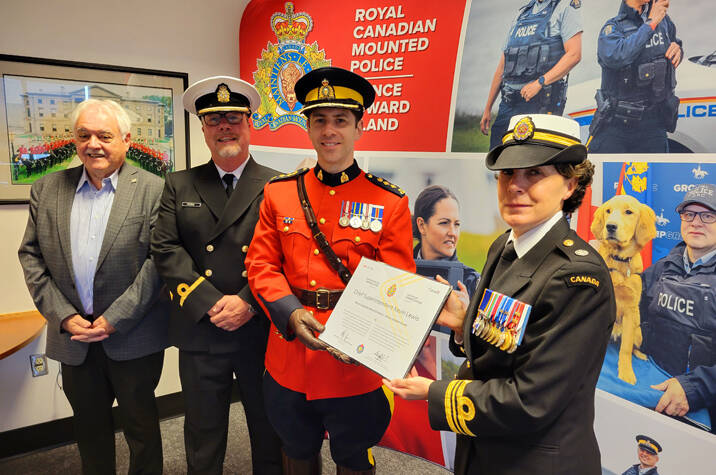 Woman in Canadian Navy uniform presents certificate to man in RCMP uniform. Two other men stand beside them, one in Canadian Navy uniform, the other in a suit.