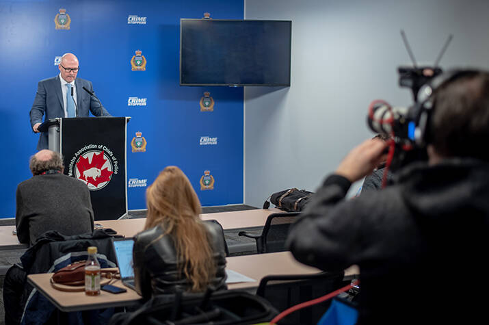 Man stands behind a podium at a press conference as reporters and photographers look on.