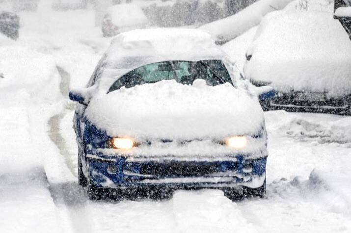 A snow-covered car drives on a snow-covered road.