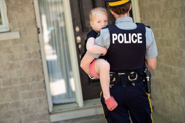 A female police officer holds a young girl in her arms standing at the front door of a house.