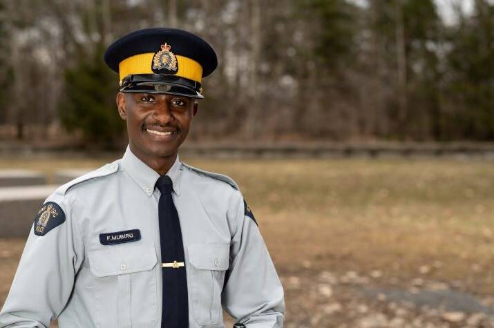 Black male <abbr>RCMP</abbr> officer stands outside smiling.