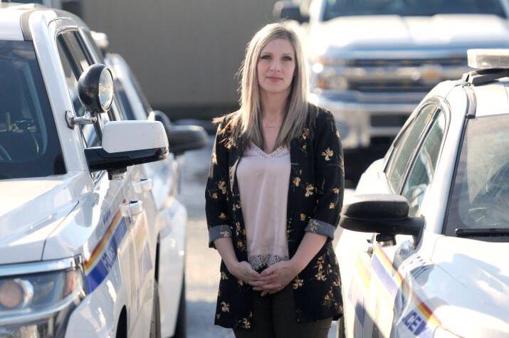 Female RCMP officer in plain clothes stands among RCMP cruisers looking at camera.
