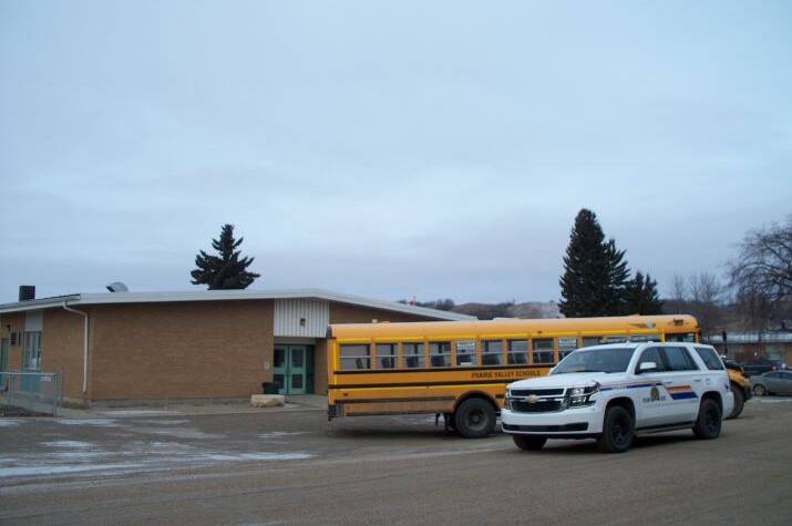 A yellow school bus is parked next to an RCMP vehicle outside of a school.
