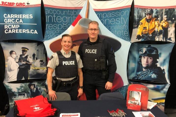 One female and one male RCMP officer stand behind a recruiting booth.