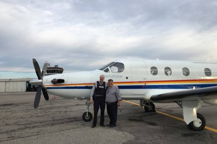 One male police officer and another man stand arm in arm and smiling in front of an airplane.