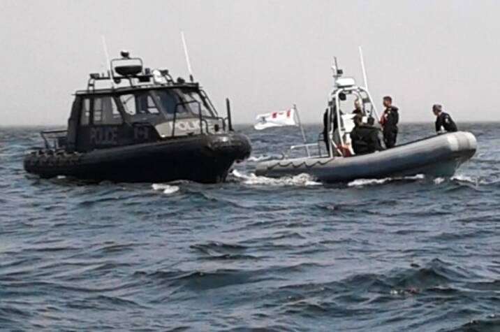 Police officers on a boat next to another boat in the ocean.