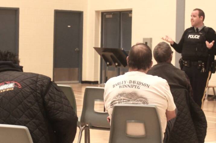 Police officer speaks to people in a school gymnasium.
