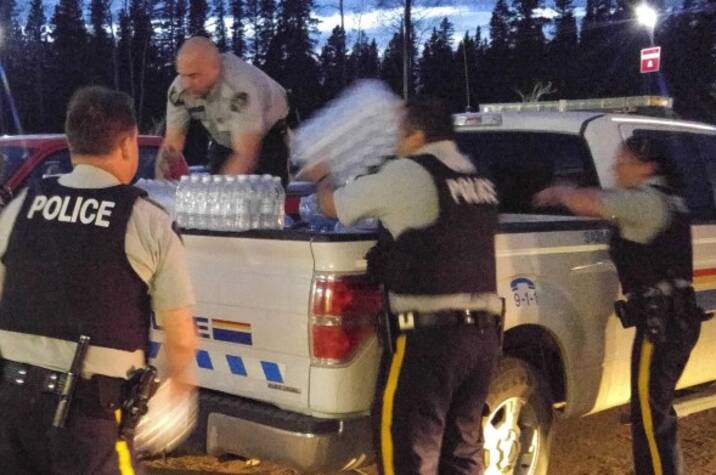 RCMP officers lift packs of water bottles off of a truck.