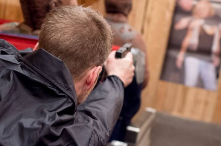 Man wearing a police jacket aims his gun at a target in an airplane aisle.