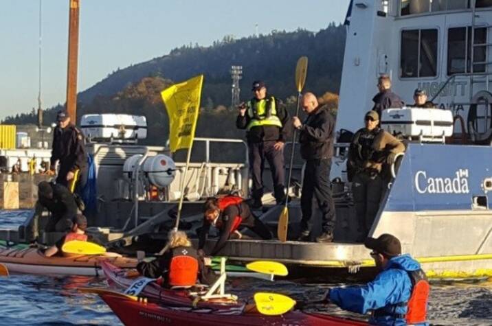 RCMP officers on vessel talk to people in kayaks in open water.