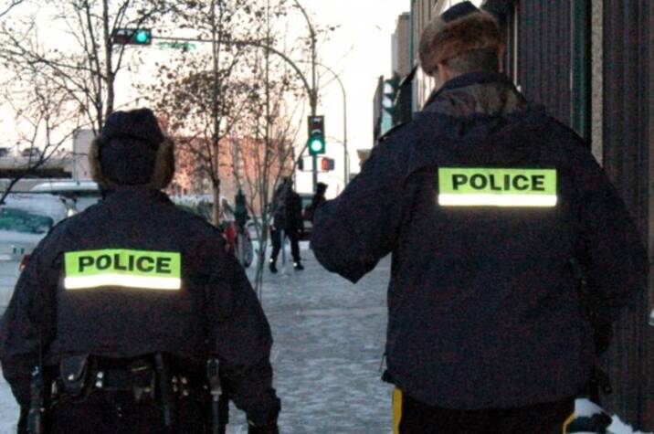 Two police officers walk on snowy sidewalk in city.