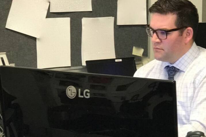 Man sits at desk behind computer.