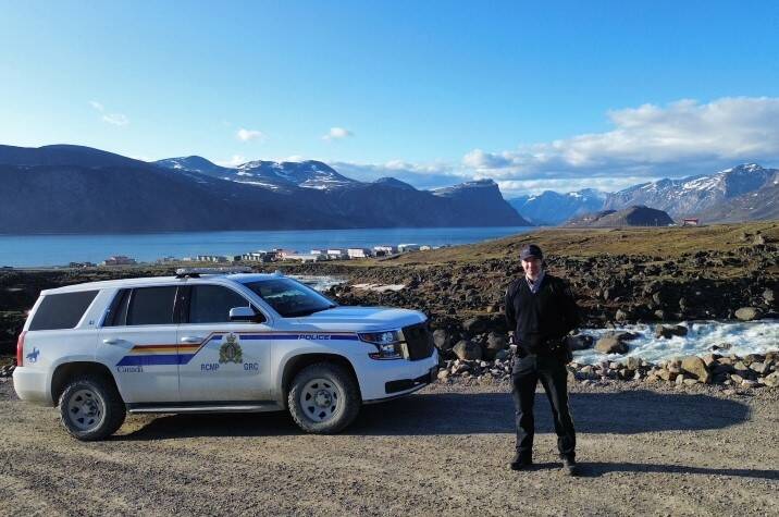 Male officer stands next to RCMP cruiser, mountain landscape in the distance.