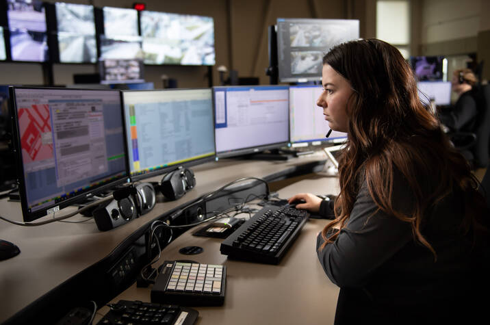 A person sits behind a computer screen with a headset on.