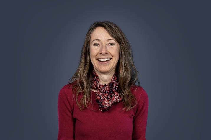 Woman in a red sweater smiles at the camera against a blue-grey background