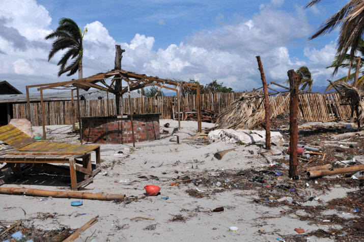 Storm torn beachfront covered in debris from garbage, fallen trees and wooden huts.