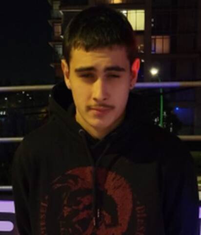 Ronin Tajali. An 18-year-old man with black hair, a black pencil thin moustache, wearing a black hoodie with a red circular logo on it.