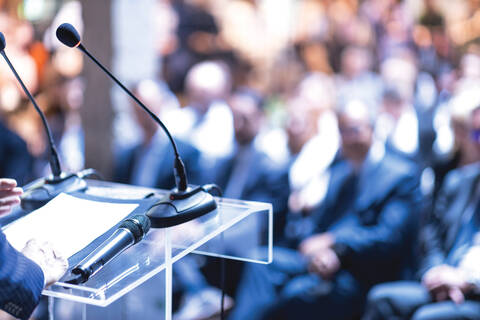 Stock photo of a speaker addressing an audience from a podium at a press conference.